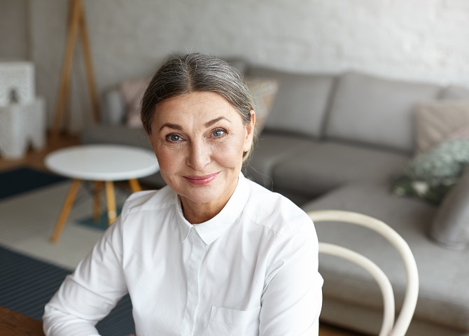 Headshot of successful positive mature 60 year old European woman life coach, consultant or psychologist in formal blouse waiting for client at home office, looking at camera with confident smile